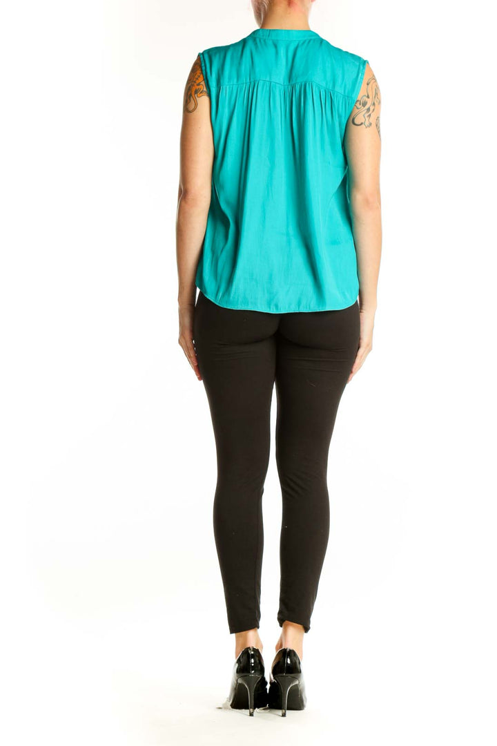 Turquoise sleeveless V-neck blouse, back view on model with black pants