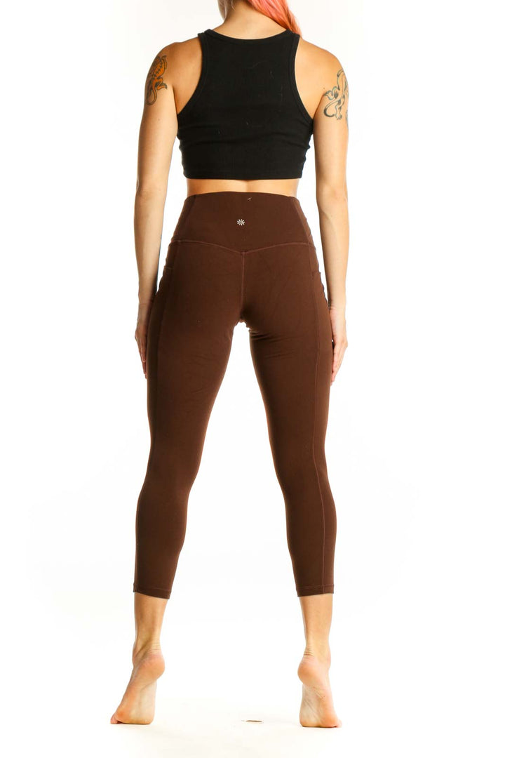 Side view of woman wearing brown Athleta capri leggings with black crop top