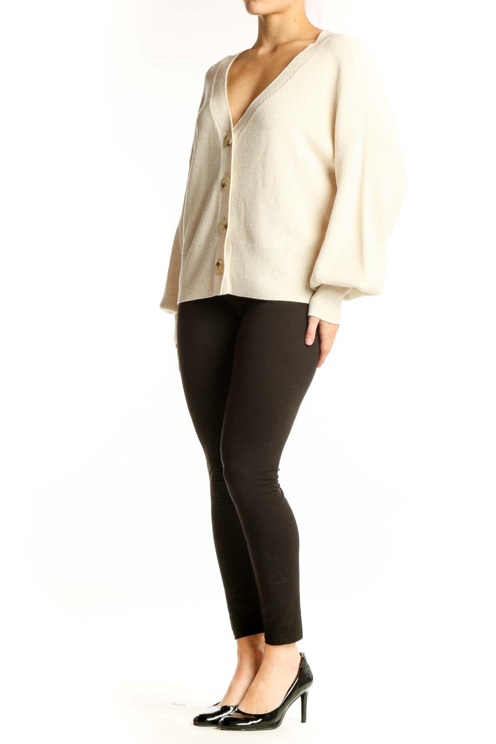 Cream ribbed button-front cardigan with puffed sleeves and gold buttons, worn with black pants
