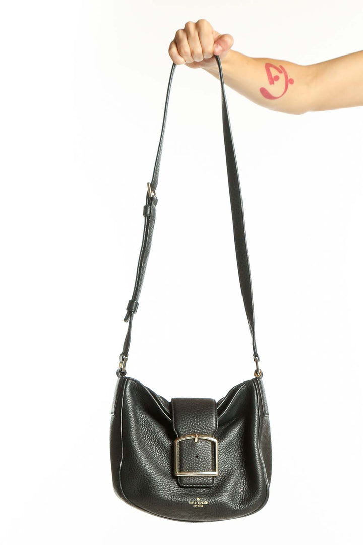 Black leather Kate Spade crossbody bag with buckle detail and adjustable shoulder strap, held by hand