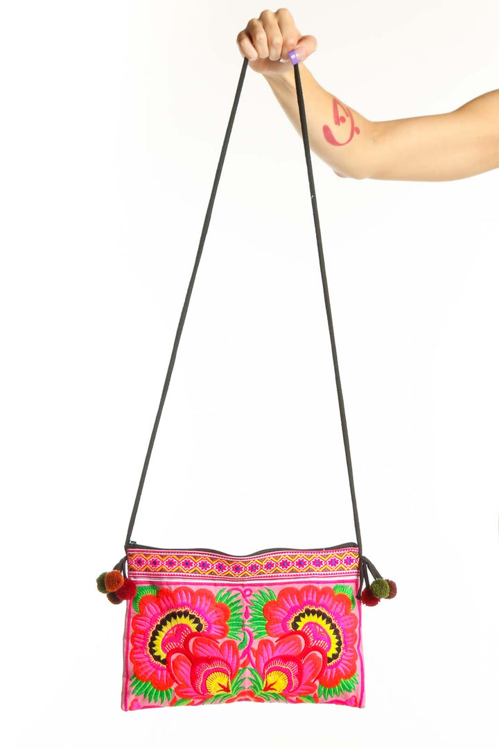 SilkRoll pink embroidered floral crossbody bag with vibrant red, yellow, and green botanical designs and pom-pom details