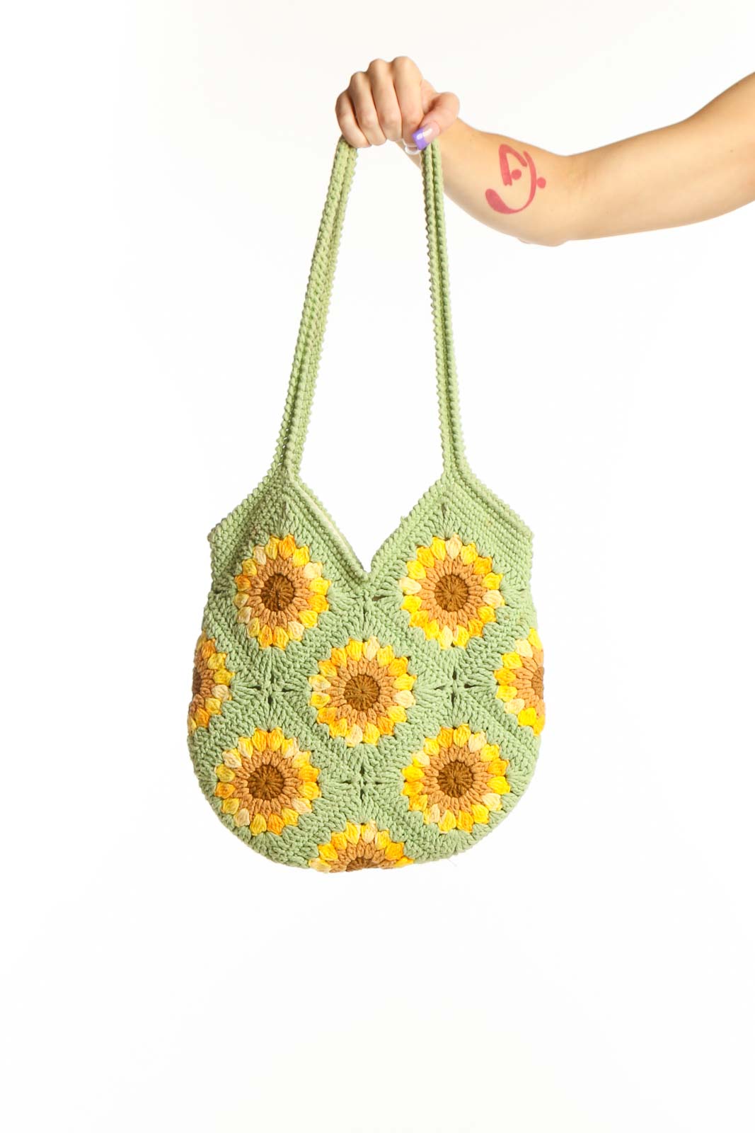 Green crochet tote bag with yellow sunflower pattern held by hand, showing front view with rope handles