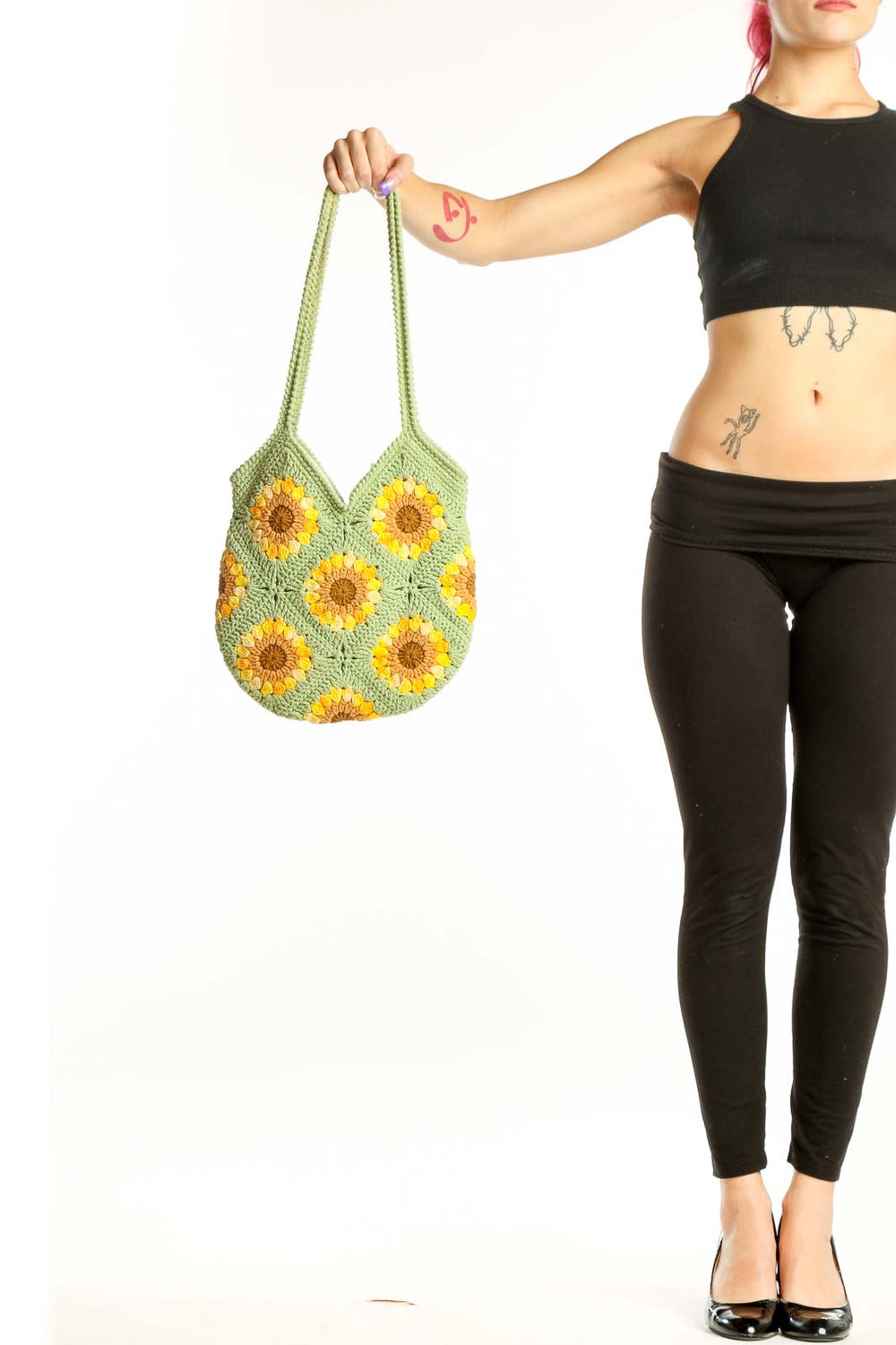 Green crochet tote bag with yellow sunflower pattern held by hand, showing front view with rope handles