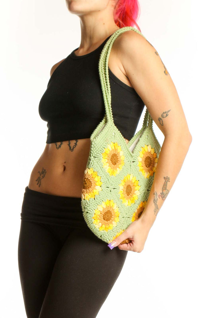 Green crochet tote bag with yellow sunflower pattern held by hand, showing front view with rope handles