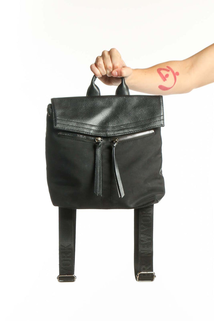 Black leather convertible backpack with metallic flap top and dual padded shoulder straps, shown being held by hand
