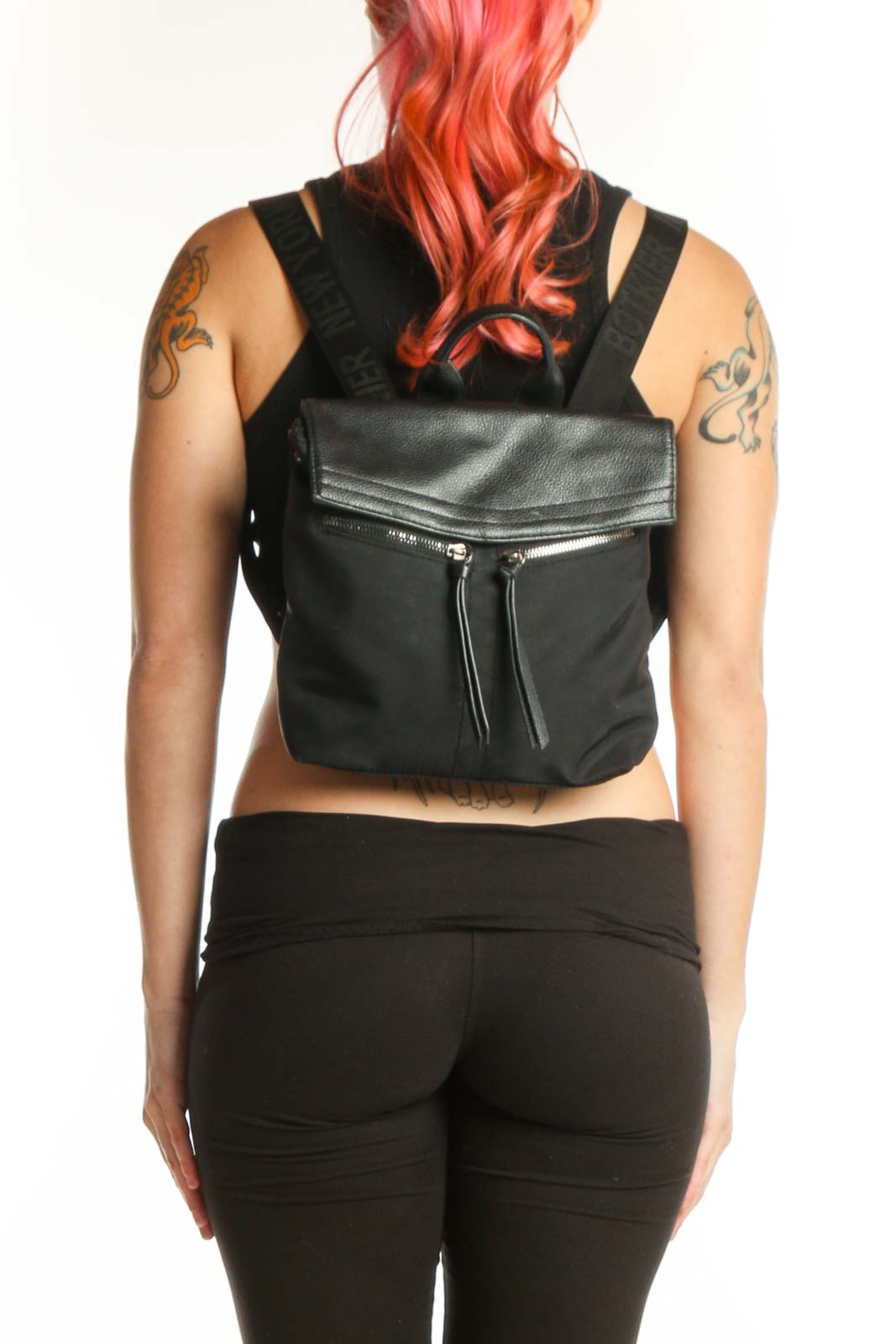 Black leather convertible backpack with metallic flap top and dual padded shoulder straps, shown being held by hand