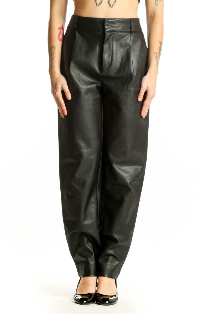 Black leather tapered pants with high waist and pleated front, worn with black platform heels