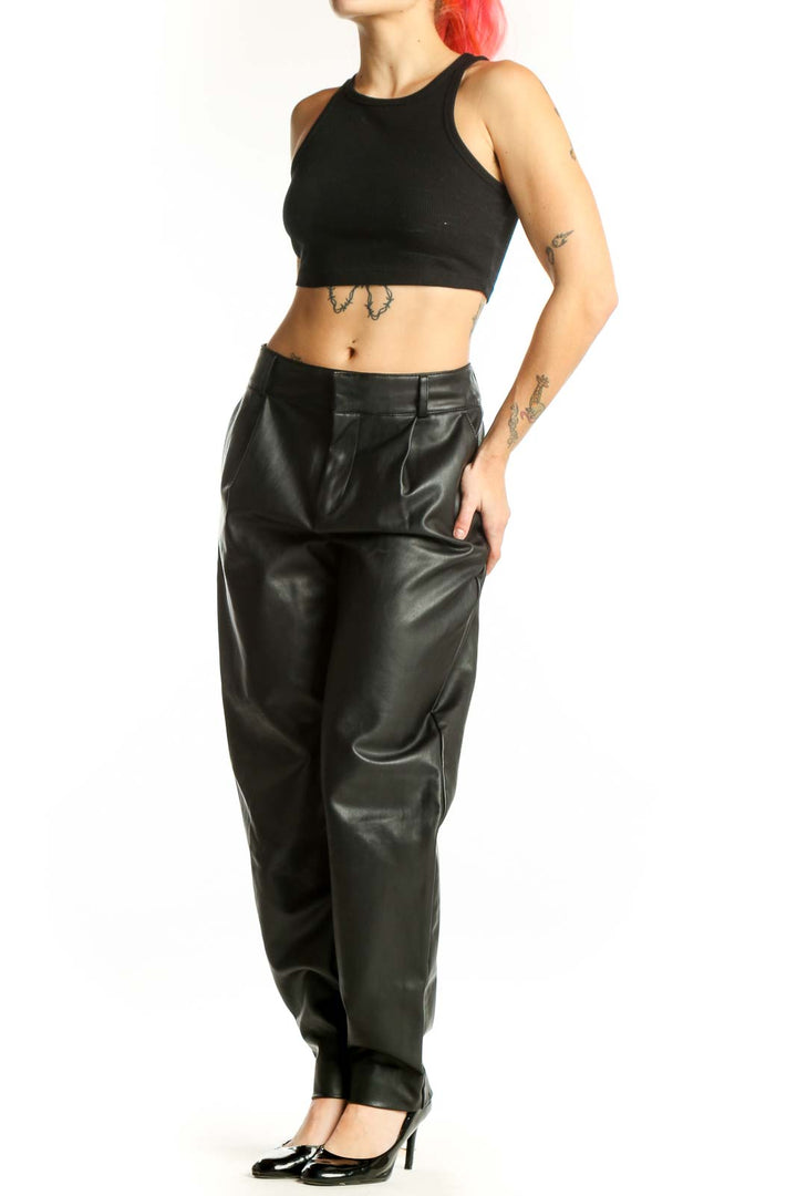 Black leather tapered pants with high waist and pleated front, worn with black platform heels