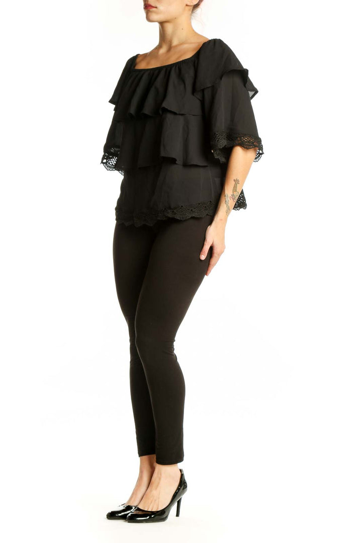 Black off-shoulder ruffled top with lace trim and layered tiers, front view on model