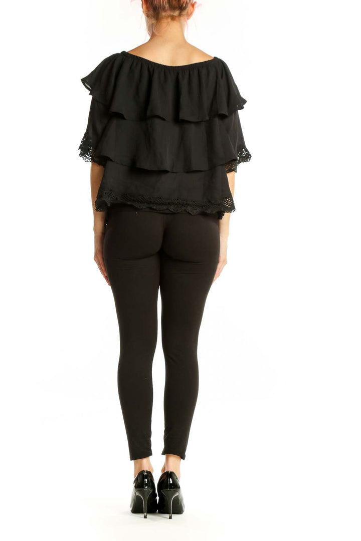 Black off-shoulder ruffled top with lace detailing, back view on model wearing black pants