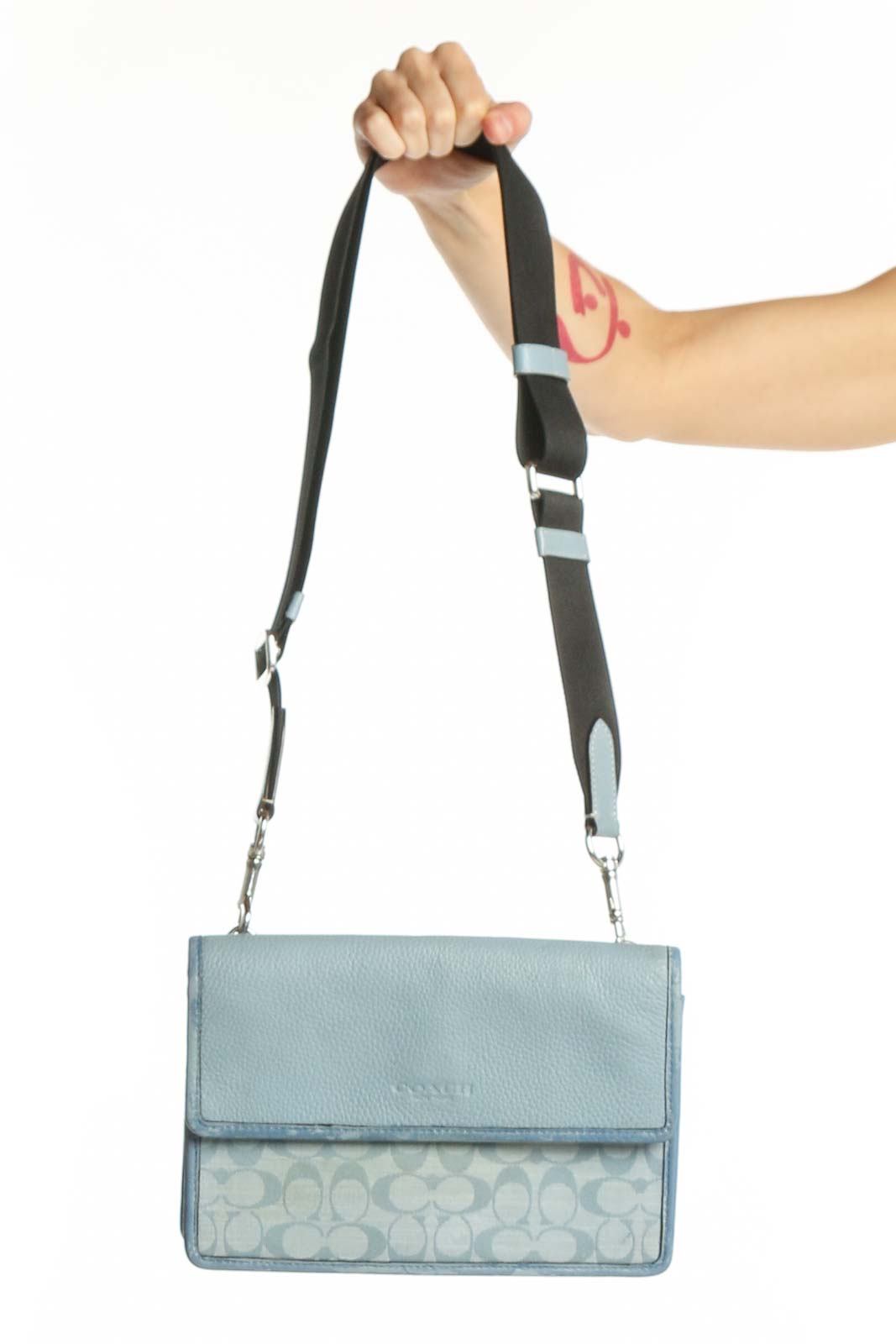 Blue Coach crossbody bag with signature pattern and black striped adjustable strap held in hand
