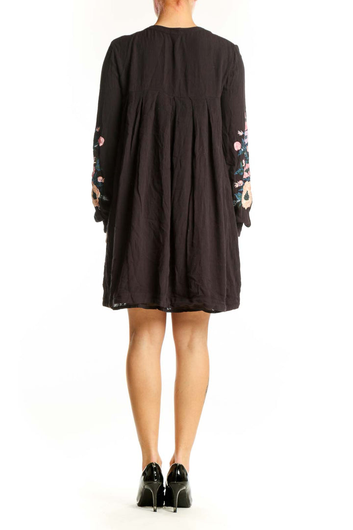 Back view of black floral embroidered dress showing high-low hem, side pockets, and full embroidery design on sleeves