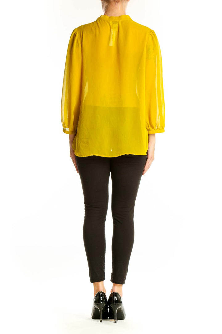 Side view of yellow sheer tie-neck blouse from LOFT with black pants