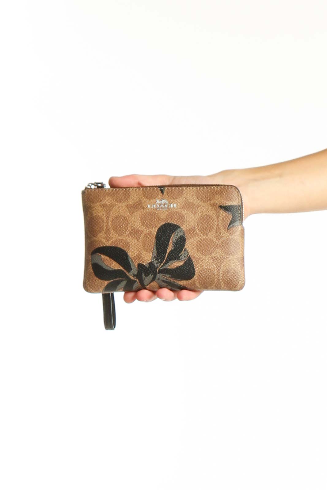 Front view of Coach brown signature canvas wristlet with black bow print