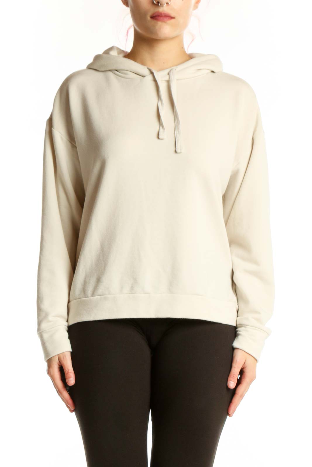 Woman wearing cream hooded sweatshirt jacket with drawstring hood and kangaroo pocket, paired with black leggings