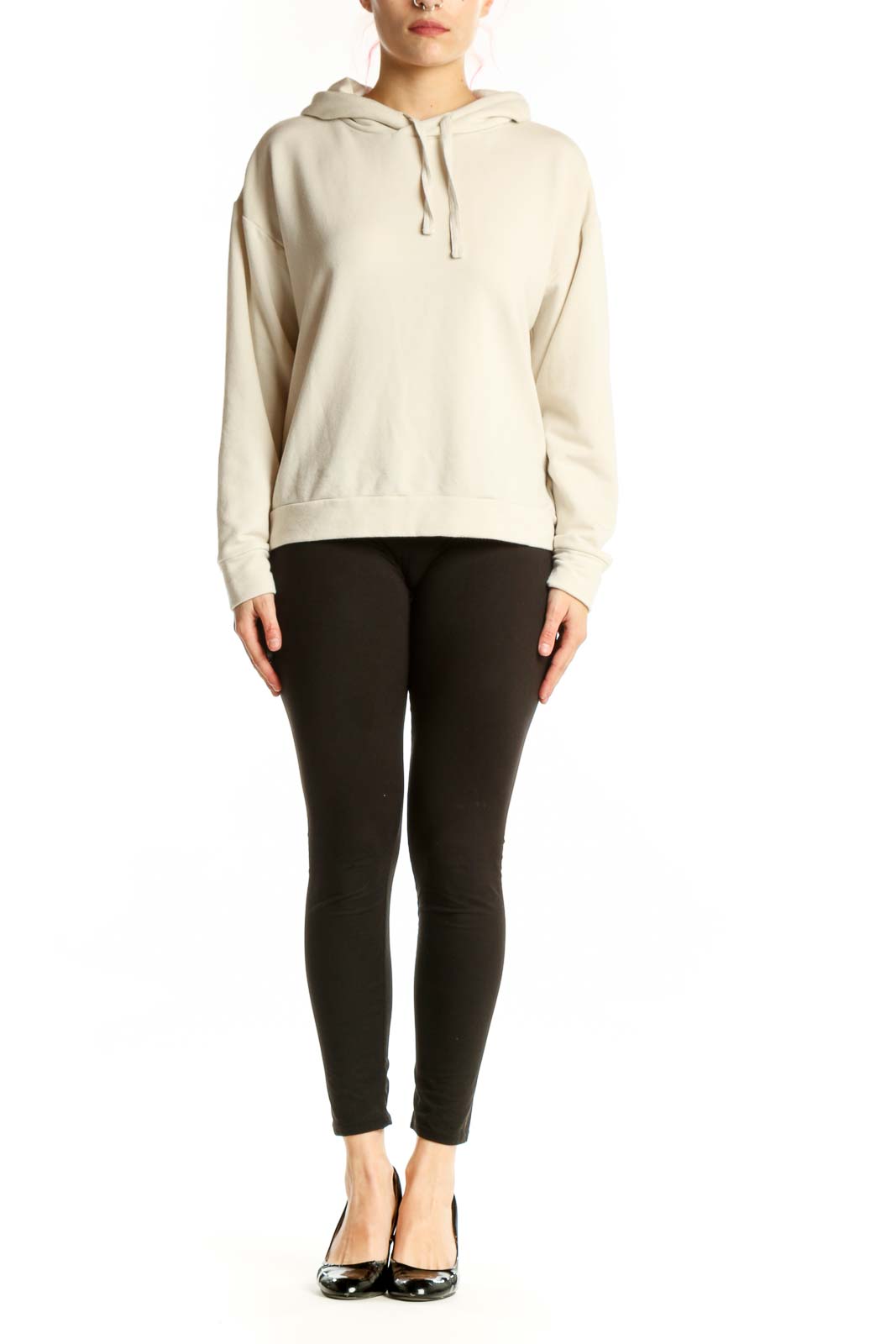Woman wearing cream hooded sweatshirt jacket with drawstring hood and kangaroo pocket, paired with black leggings