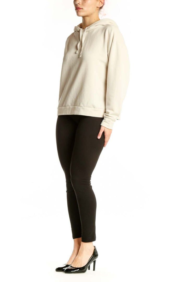 Woman wearing cream hooded sweatshirt jacket with drawstring hood and kangaroo pocket, paired with black leggings