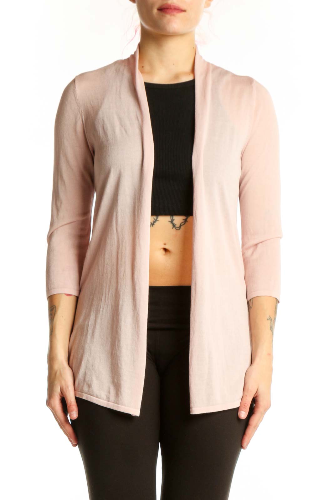 Woman wearing blush pink open front cardigan over black top, styled with black pants