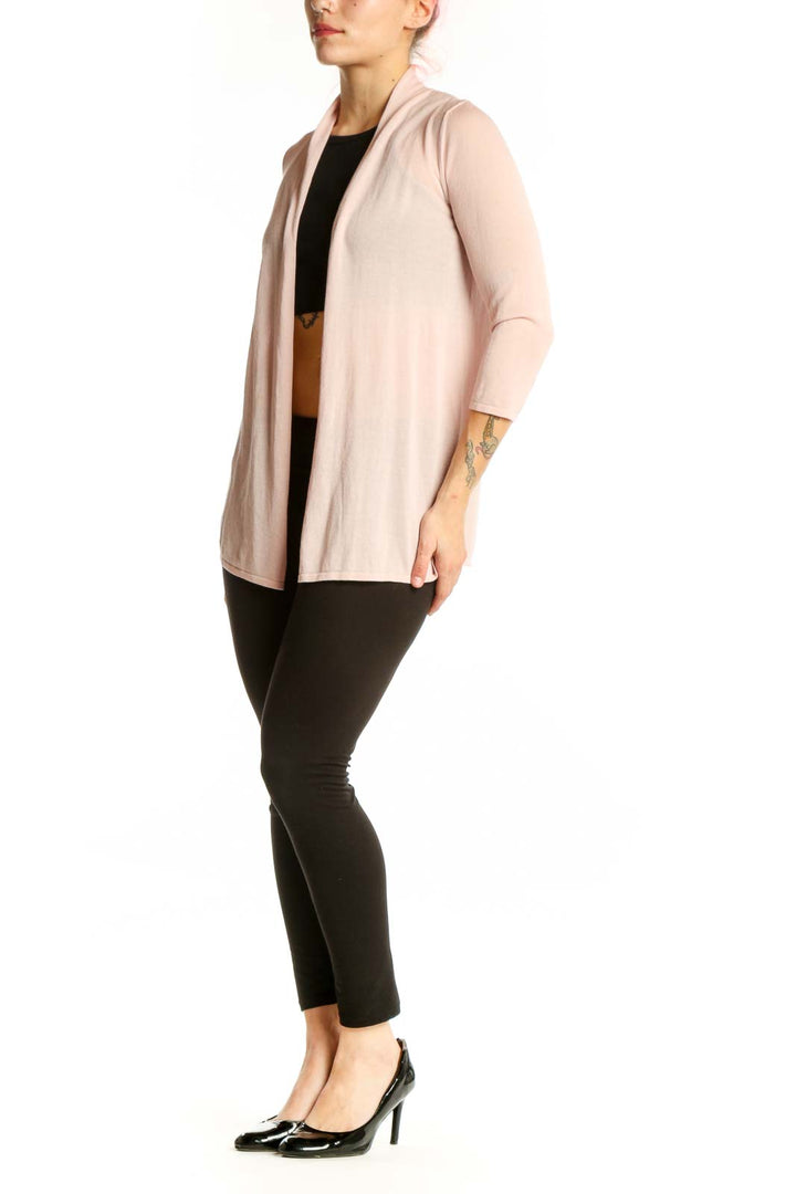 Woman wearing blush pink open front cardigan over black top, styled with black pants