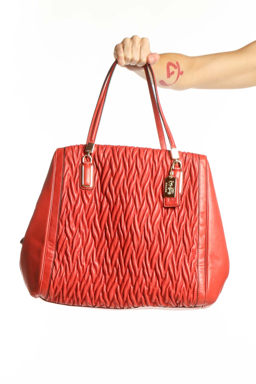 Red quilted Coach shoulder bag with dual handles and signature charm details, displayed on model's arm