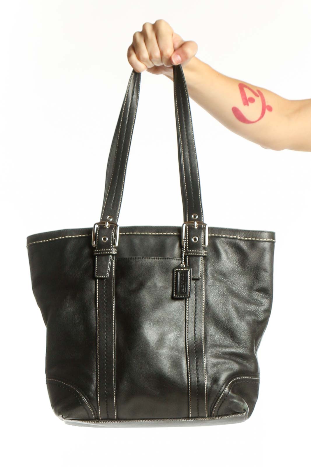 Black leather Coach satchel tote with white contrast stitching and dual handles held by model