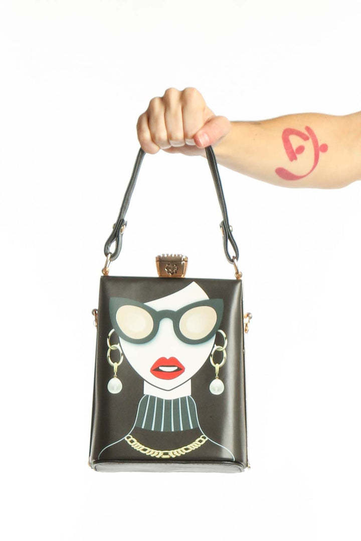 Black SilkRoll crossbody clutch with illustrated fashion portrait featuring woman in oversized sunglasses, red lips, and gold chain details