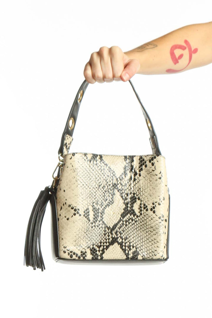 Cream and black python print crossbody bag with adjustable strap and tassel detail held by hand