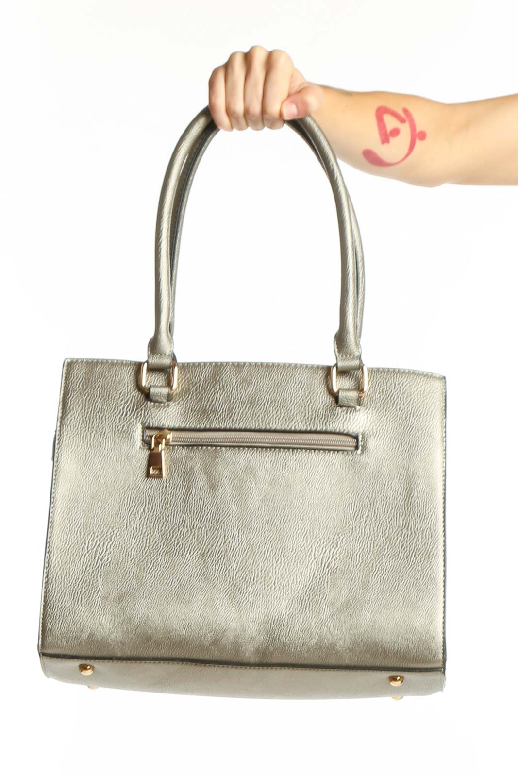 Silver metallic tote bag with dual handles and gold hardware, held by a woman's hand