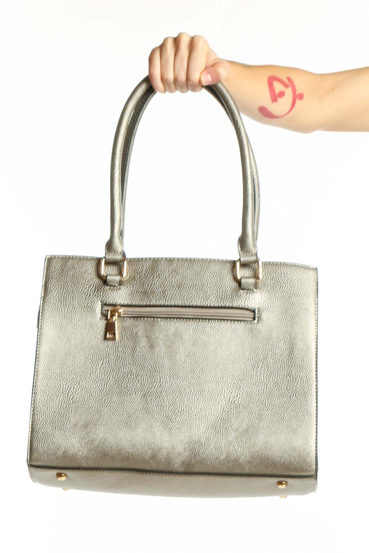 Silver metallic tote bag with dual handles and gold hardware, held by a woman's hand