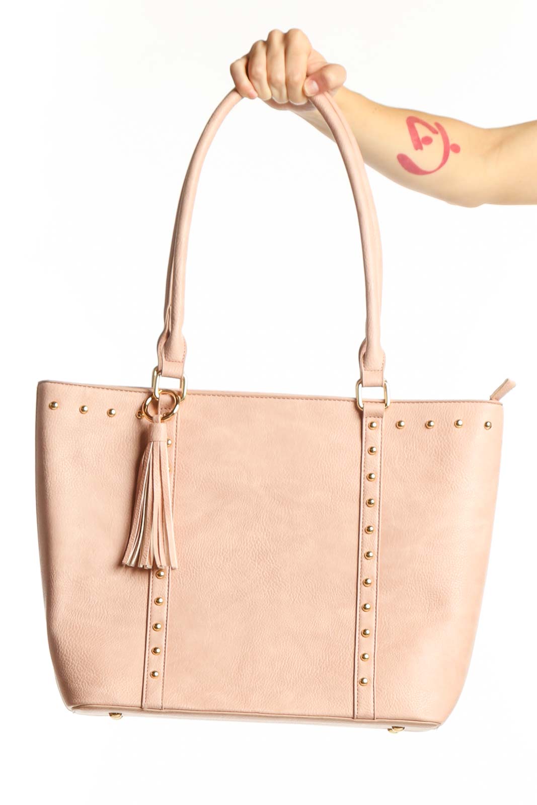 Blush pink studded tote bag with gold studs, dual handles, and tassel detail held by model