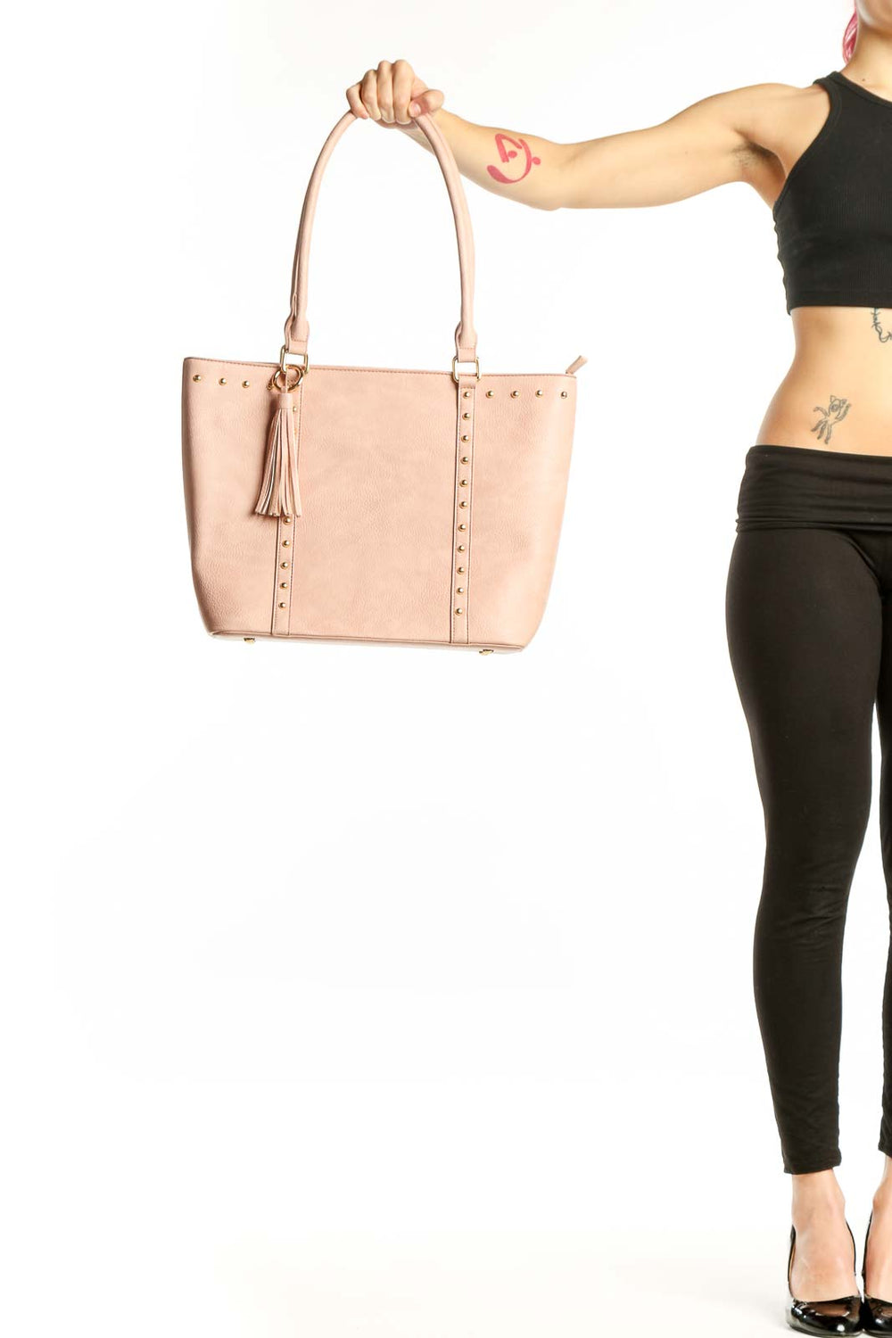Blush pink studded tote bag with gold studs, dual handles, and tassel detail held by model