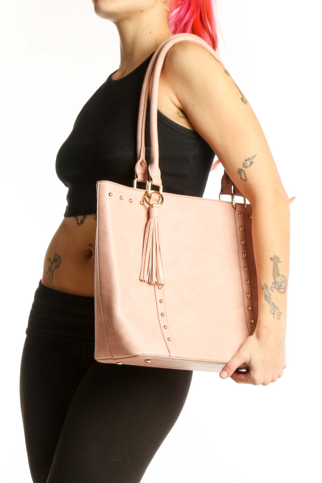 Blush pink studded tote bag with gold studs, dual handles, and tassel detail held by model