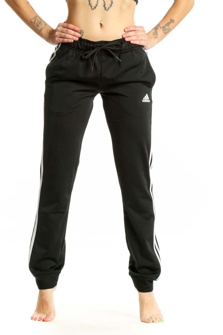 Black Adidas striped jogger pants with white three-stripe detail, drawstring waistband, and tapered ankles, front view