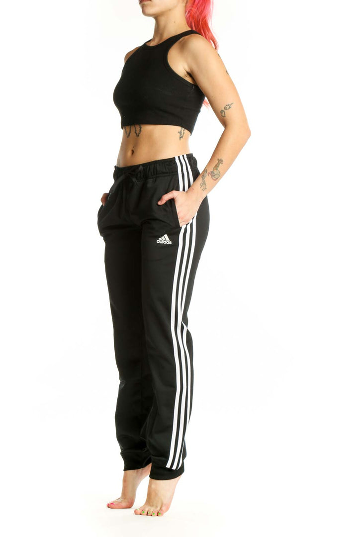 Black Adidas striped jogger pants with white three-stripe detail, drawstring waistband, and tapered ankles, front view