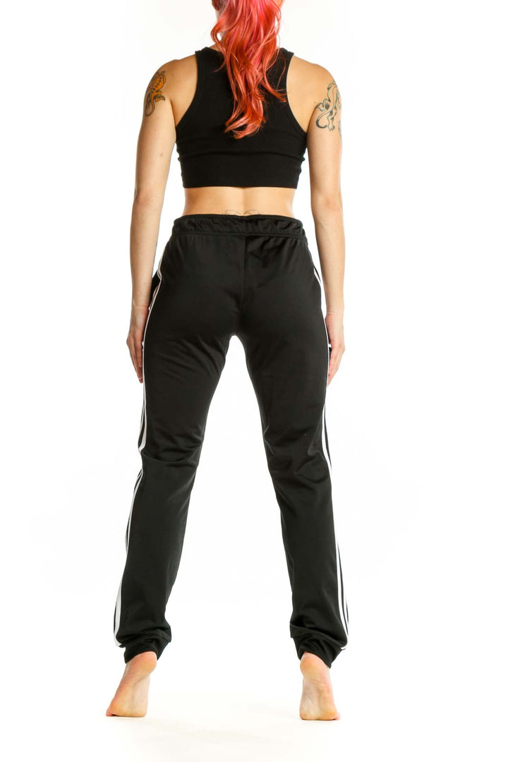 Black Adidas striped jogger pants with white side stripes and functional pockets, side view on model