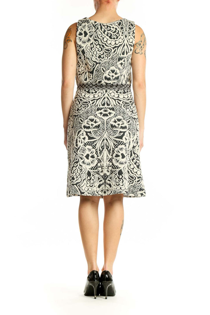 Back view of cream and black ornamental print sleeveless dress showing fitted bodice and flowing skirt