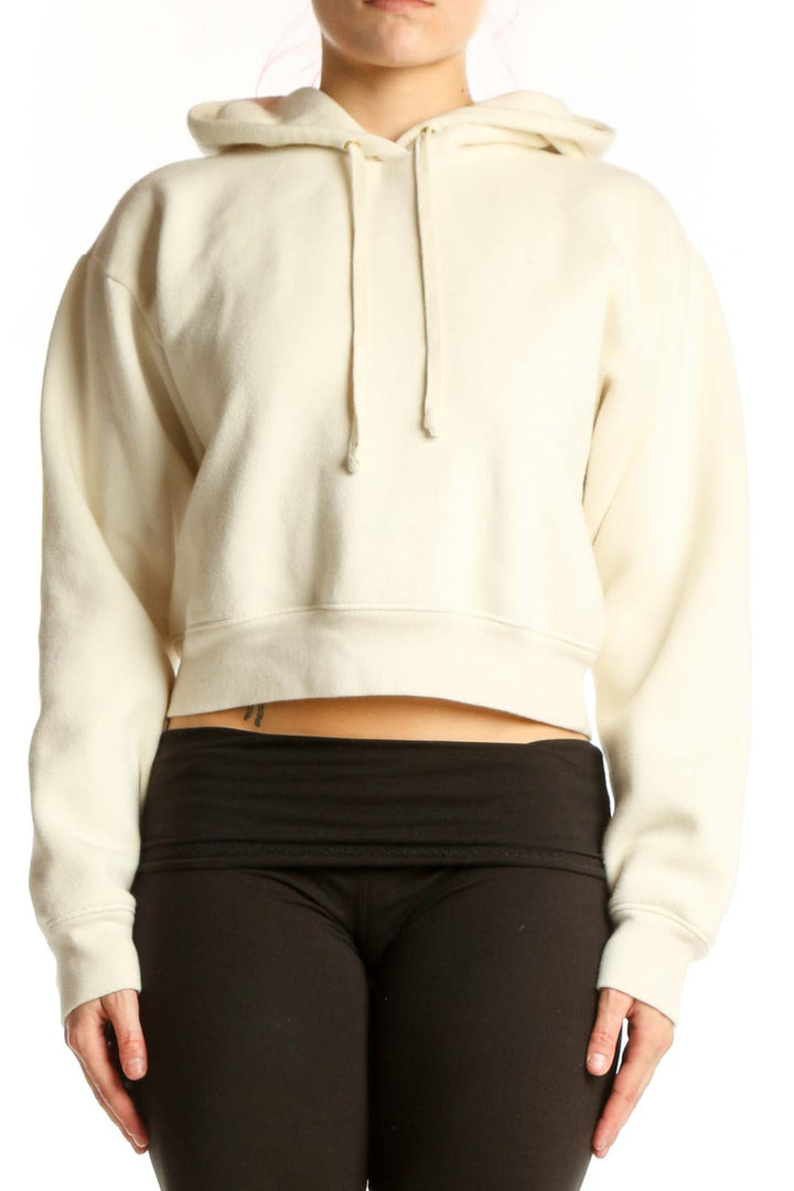 Front view of cream cropped hoodie with drawstring hood and long sleeves on model wearing black pants