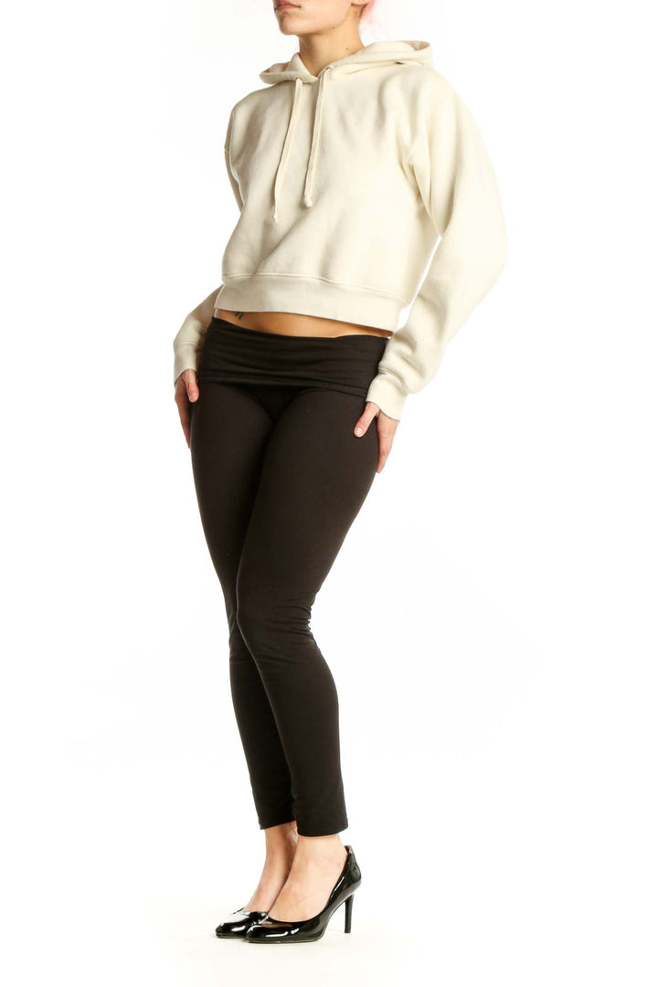 Front view of cream cropped hoodie with drawstring hood and long sleeves on model wearing black pants