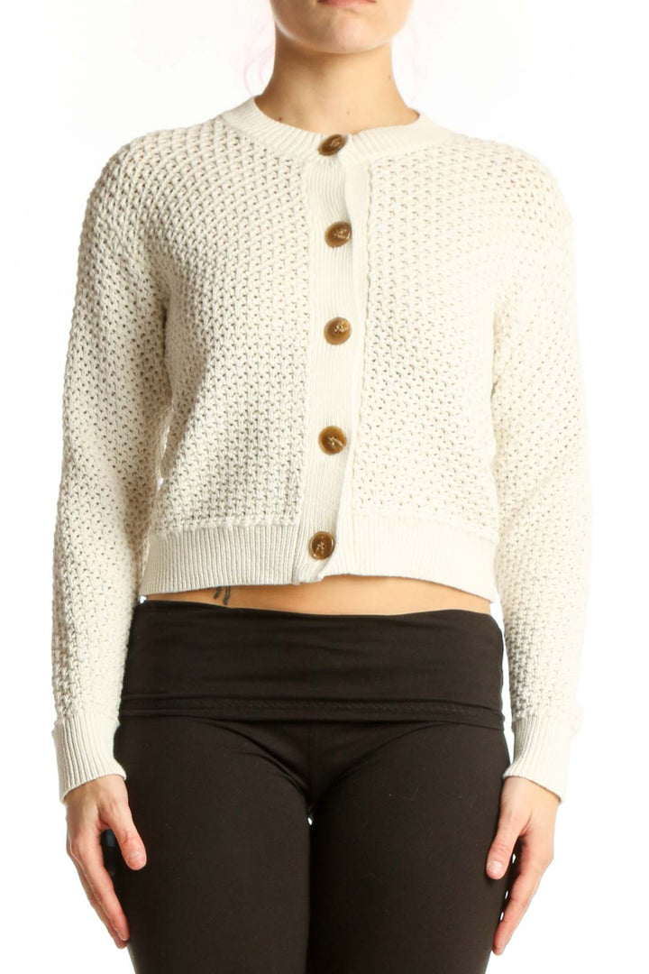 Cream textured knit cardigan with wood-tone button front and cropped silhouette, worn with black pants