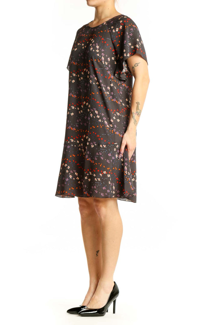 Black floral short sleeve Cabi dress with red, orange, and cream scattered blooms, front view on model