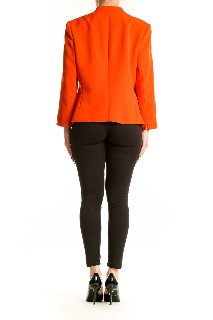 Orange blazer back view showing structured fit and peplum detail, paired with black pants and heels