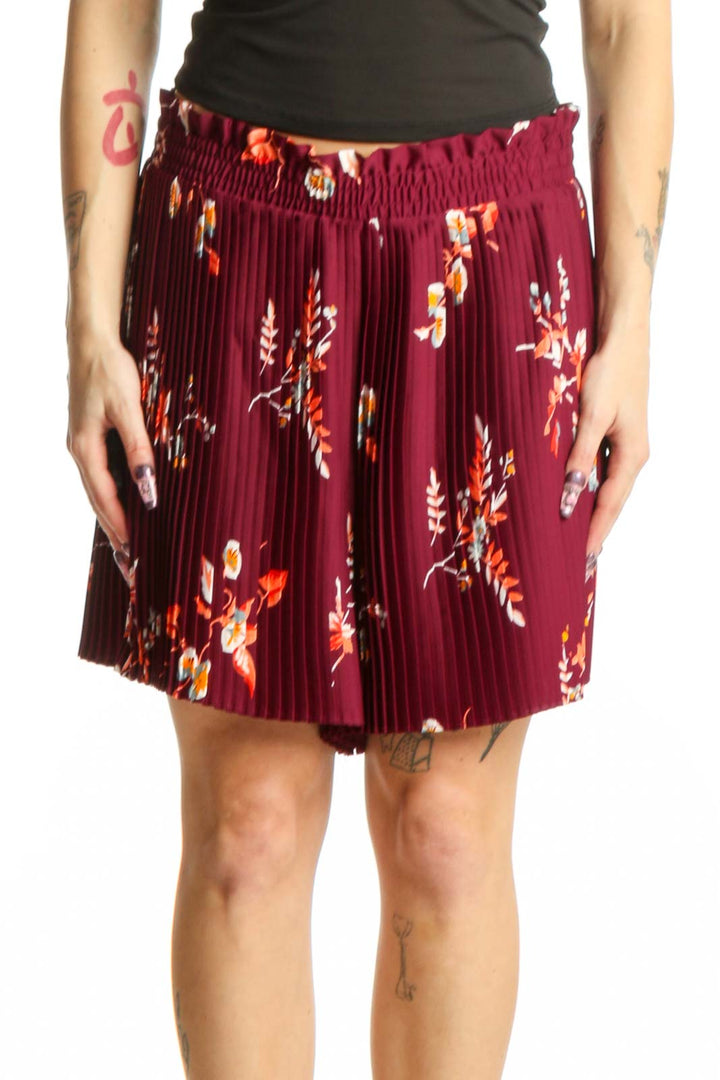 Front view of burgundy floral pleated shorts with orange and yellow botanical print, elastic waistband, and knee-length cut