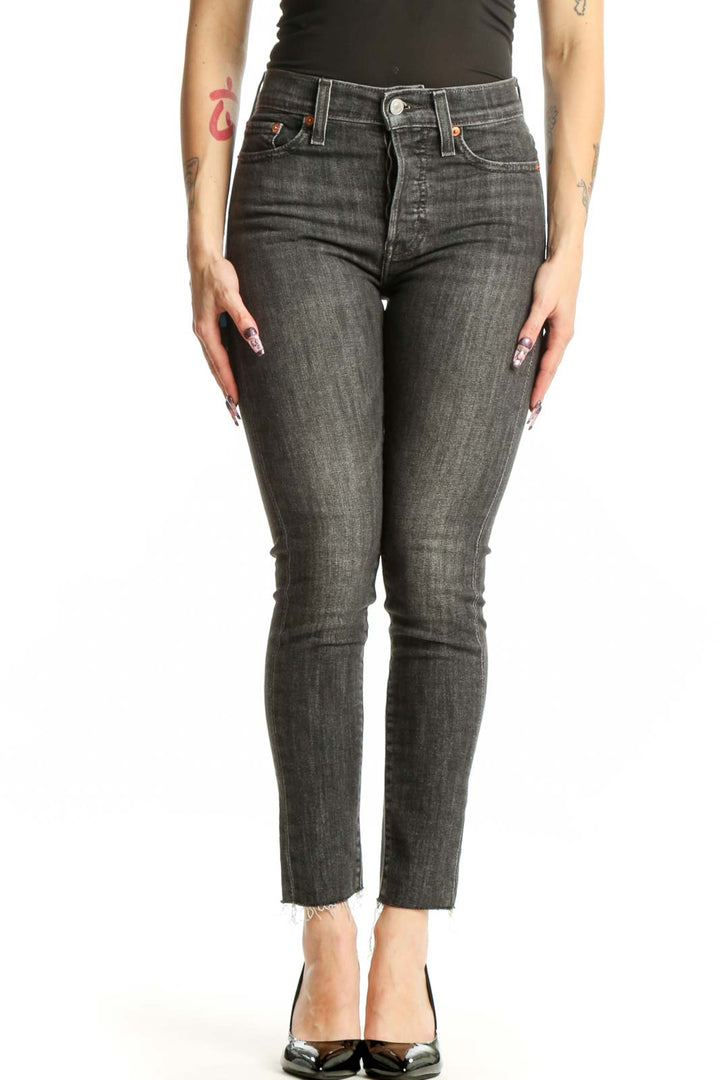 Front view of gray cropped skinny Levi's jeans with distressed hem on model wearing black top