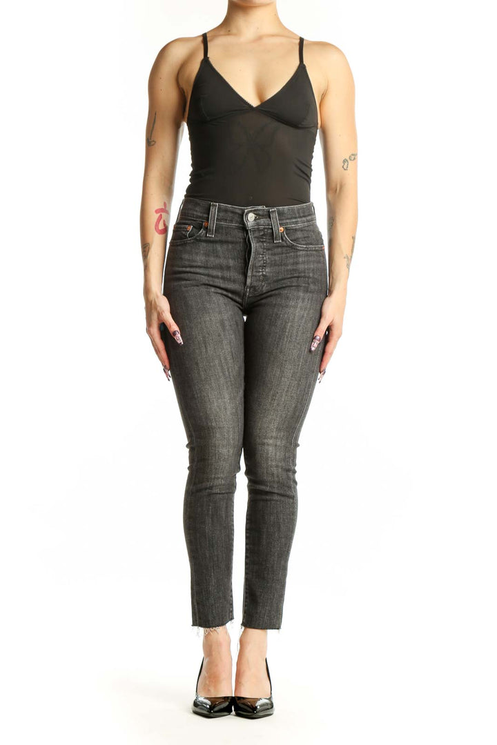 Front view of gray cropped skinny Levi's jeans with distressed hem on model wearing black top