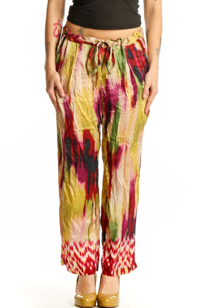 Front view of multicolor silk ikat print pants with vibrant red, yellow, pink, and green watercolor pattern and geometric hem detail