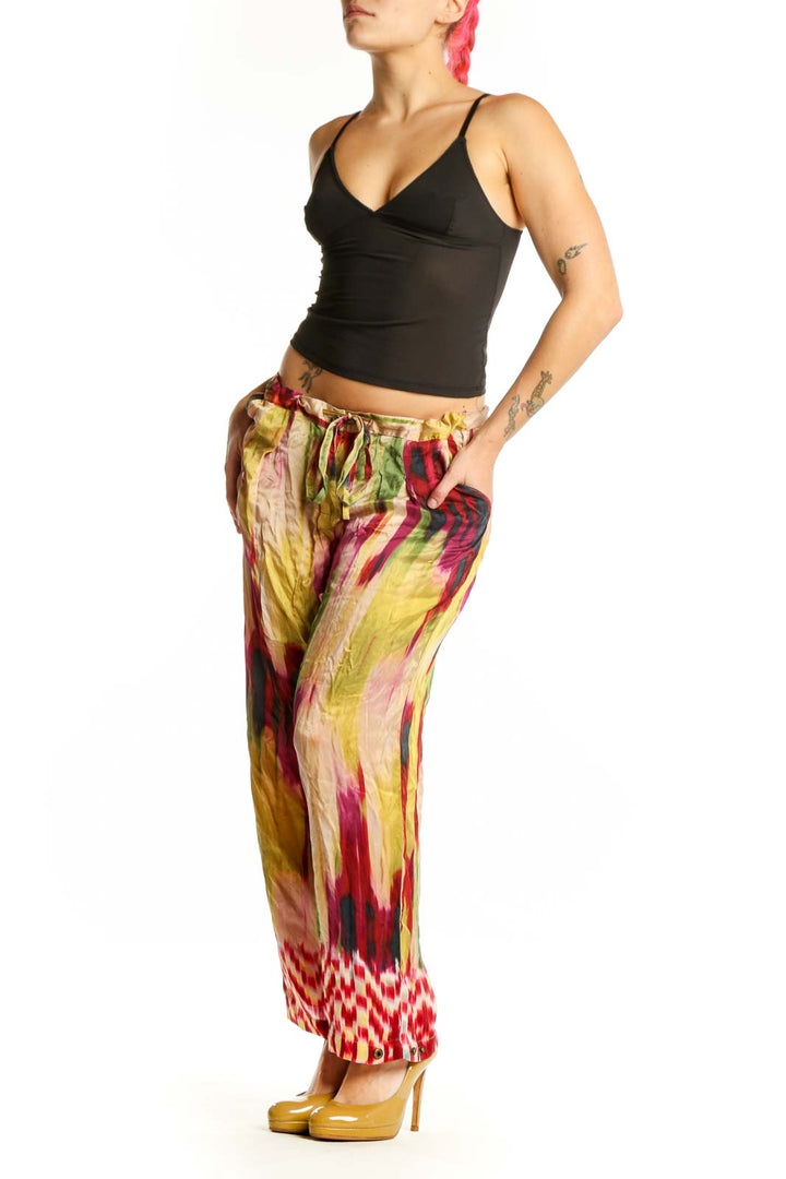 Front view of multicolor silk ikat print pants with vibrant red, yellow, pink, and green watercolor pattern and geometric hem detail