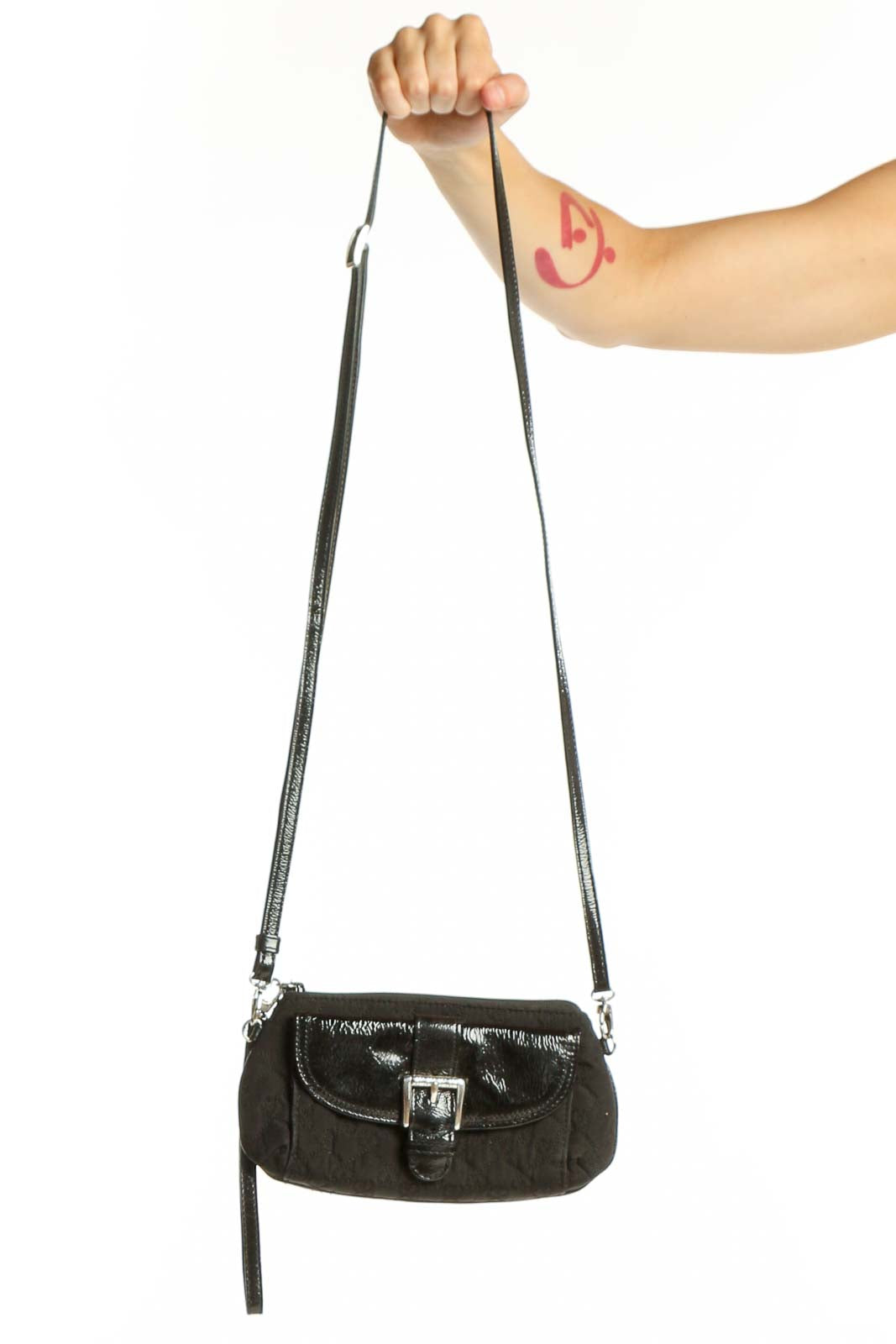 Black leather crossbody bag by Brighton with adjustable strap held in hand, showing front flap closure and silver hardware