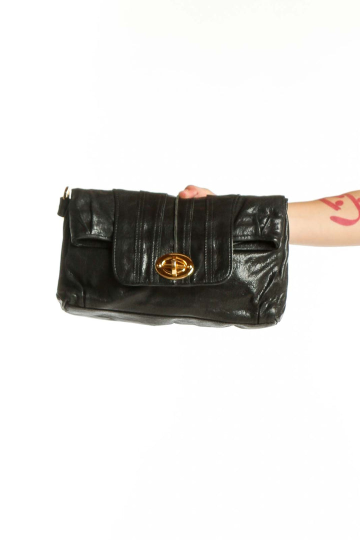 Black quilted leather clutch with gold-tone turnlock closure held in hand