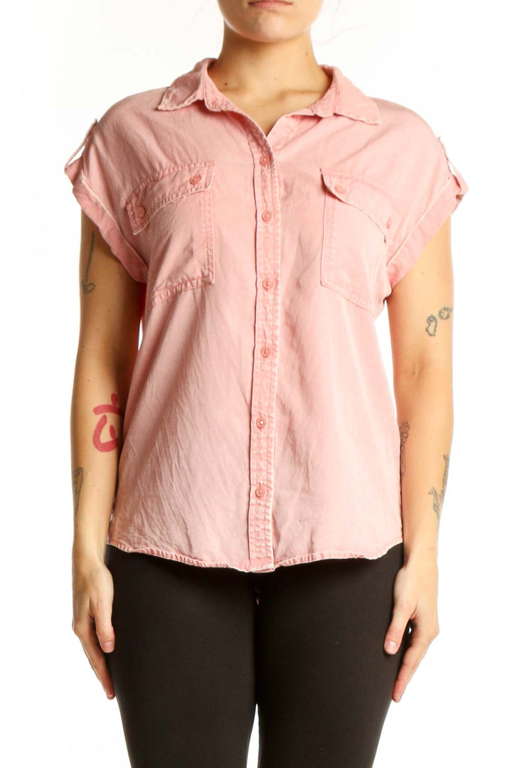 Pink short-sleeve button-up shirt with collared neckline and front pockets, worn with black pants