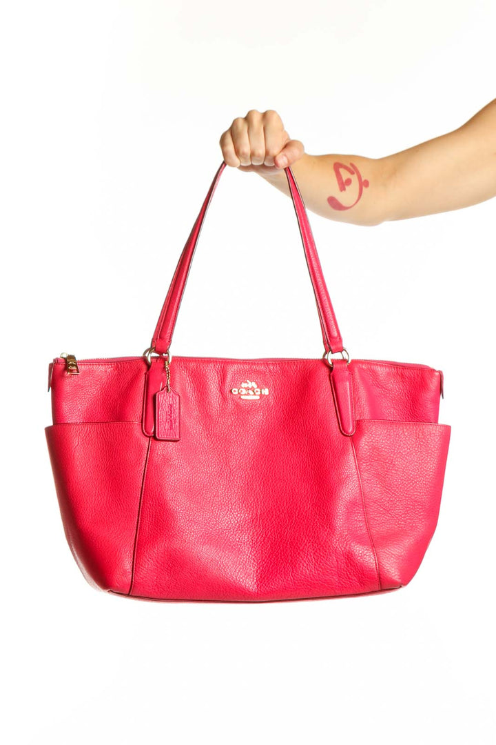 Pink Coach leather shoulder tote bag with dual straps and Coach logo hardware, held by a woman's hand